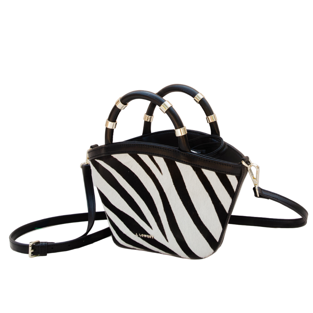 Black and white zebra-striped handbag with gold accents on a beige background
