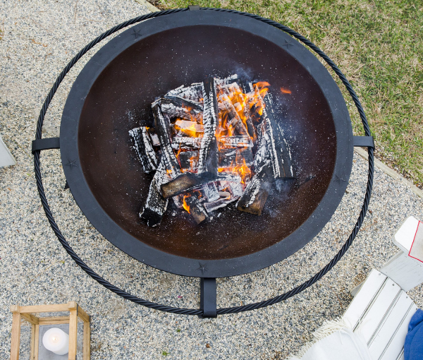 Fire pit with burning wood and a 50-gallon label on a concrete surface.