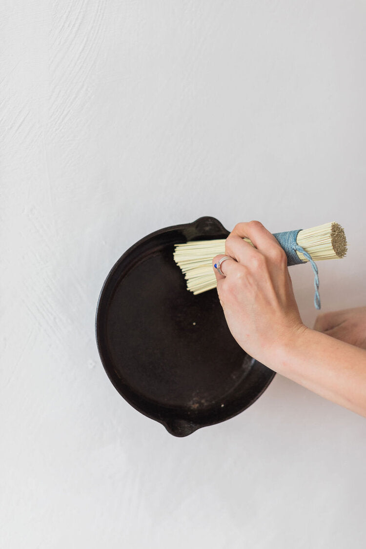 Person cleaning a black cast iron skillet with a brush on a white background
