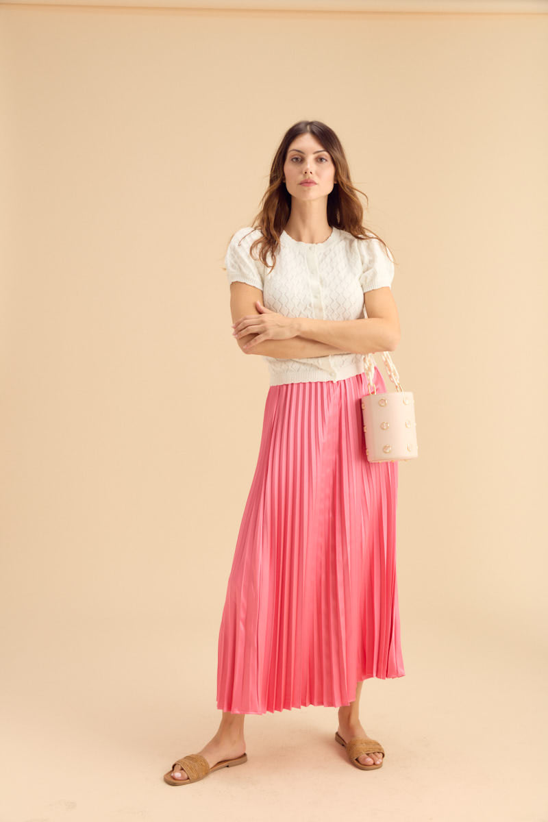 Woman in white top and pink pleated skirt against a beige background