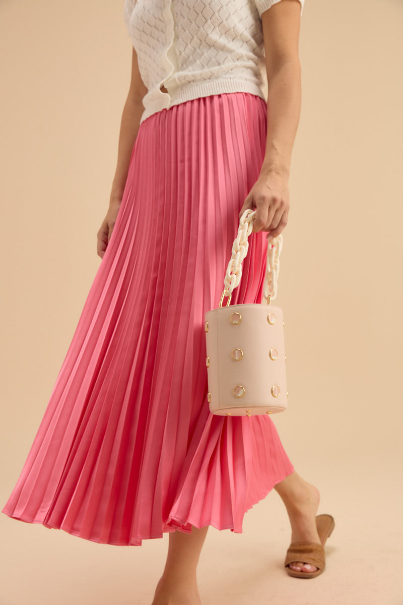 Person wearing a pink pleated skirt holding a cream handbag against a beige background.
