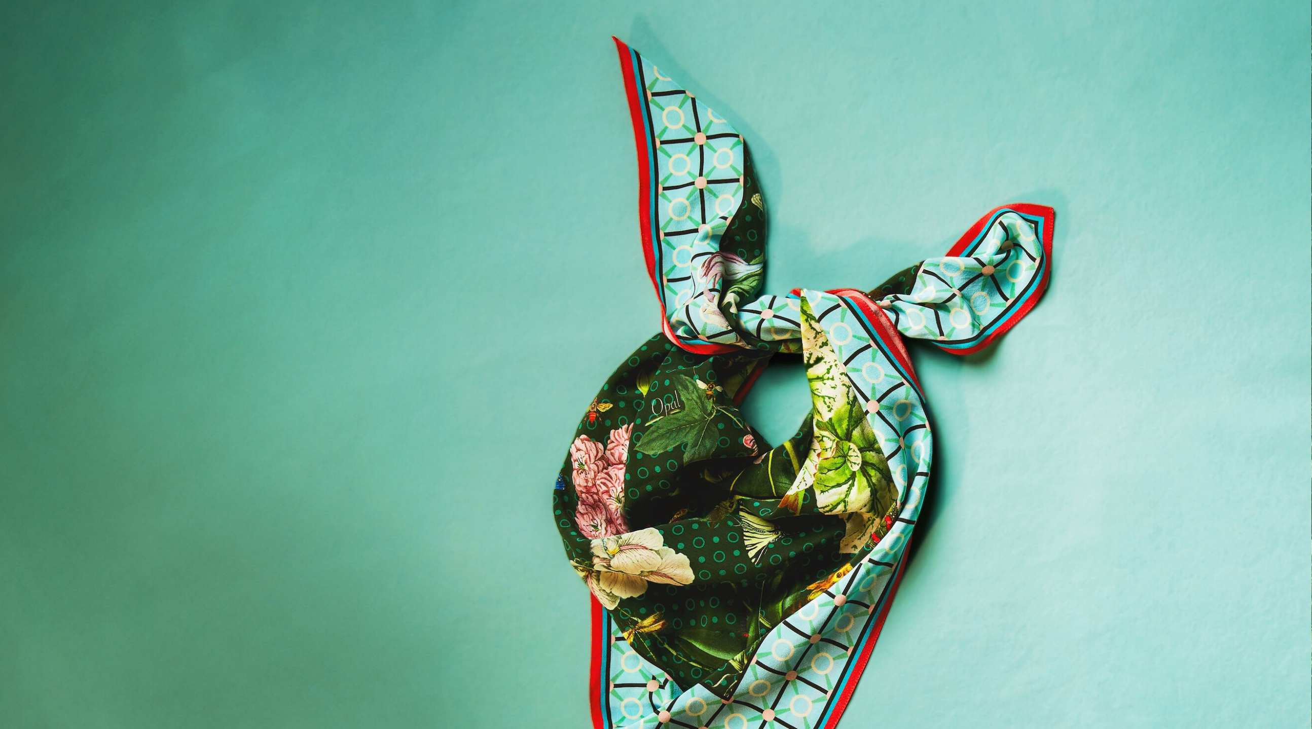 A colorful silk scarf is artistically tied on a teal background.