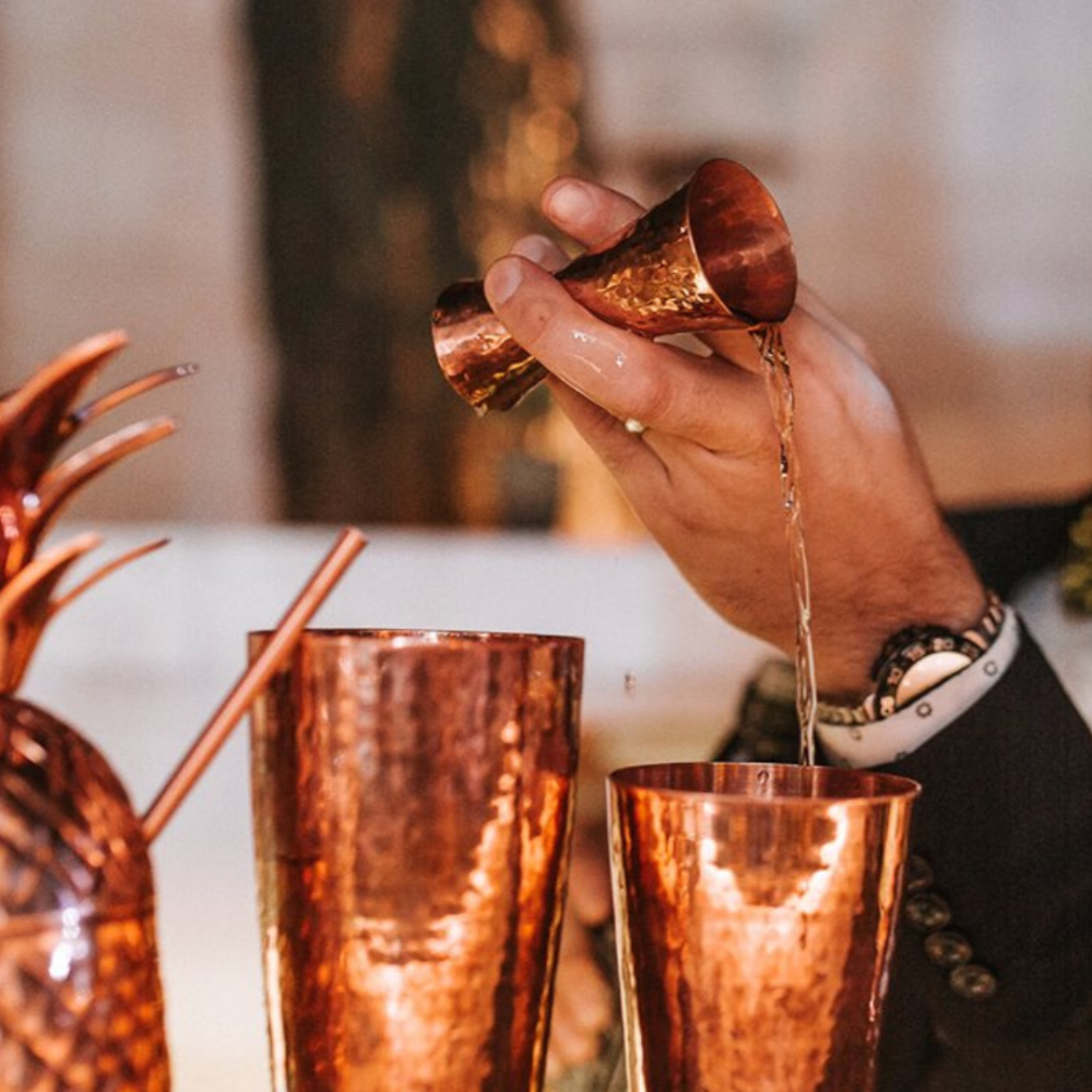 Cocktail being poured into a copper shaker with a blurred background