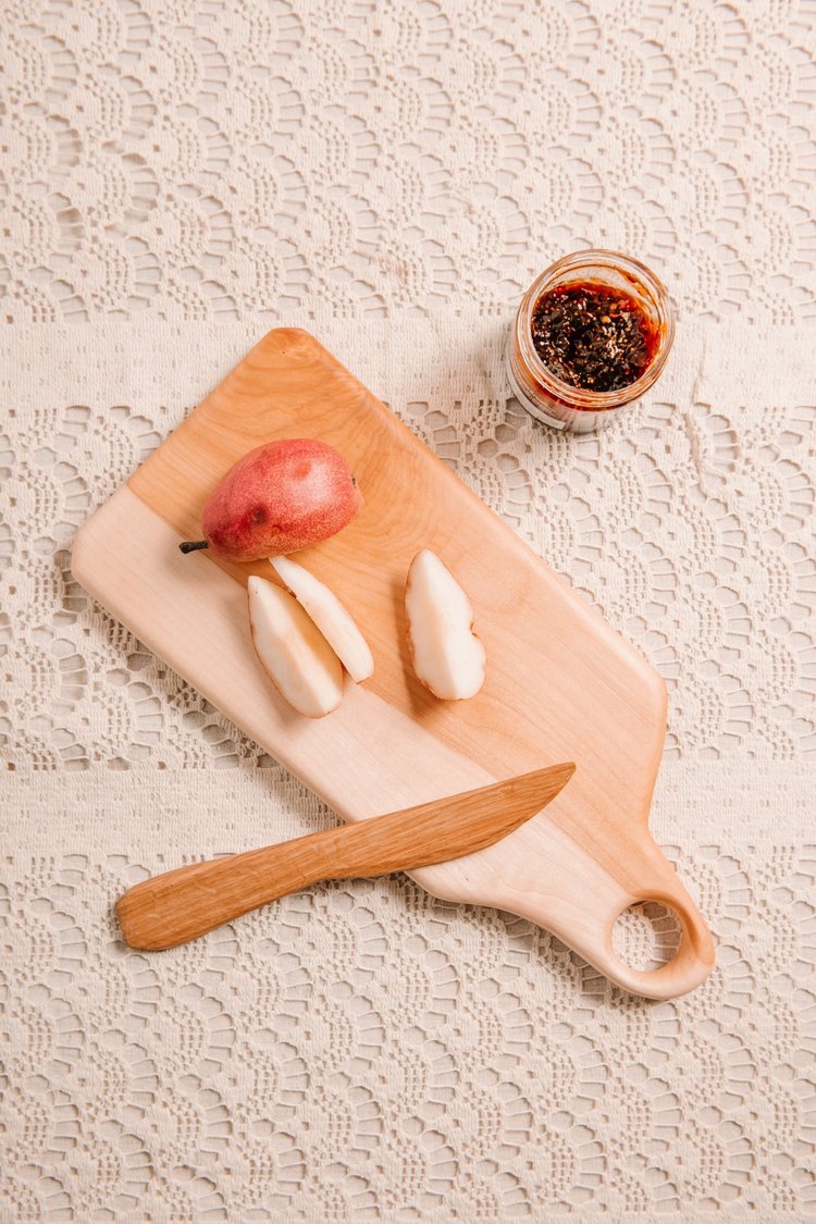 Wooden cutting board with apple, knife, and jar of jam on lace tablecloth