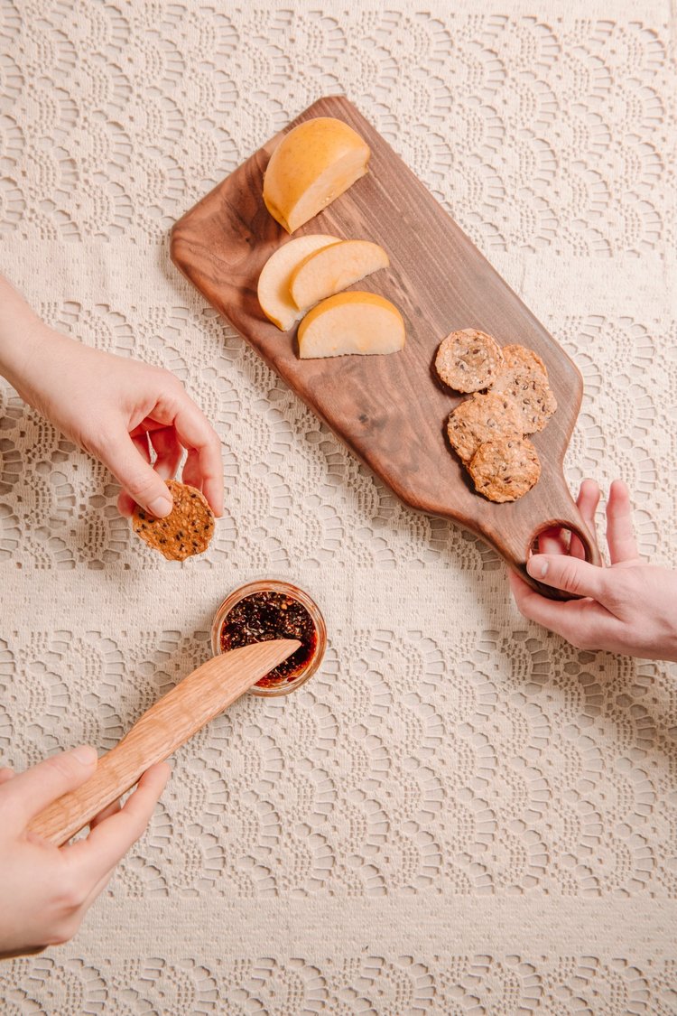 Three people sharing a wooden board with cheese, crackers, and a small container of what appears to be chutney.