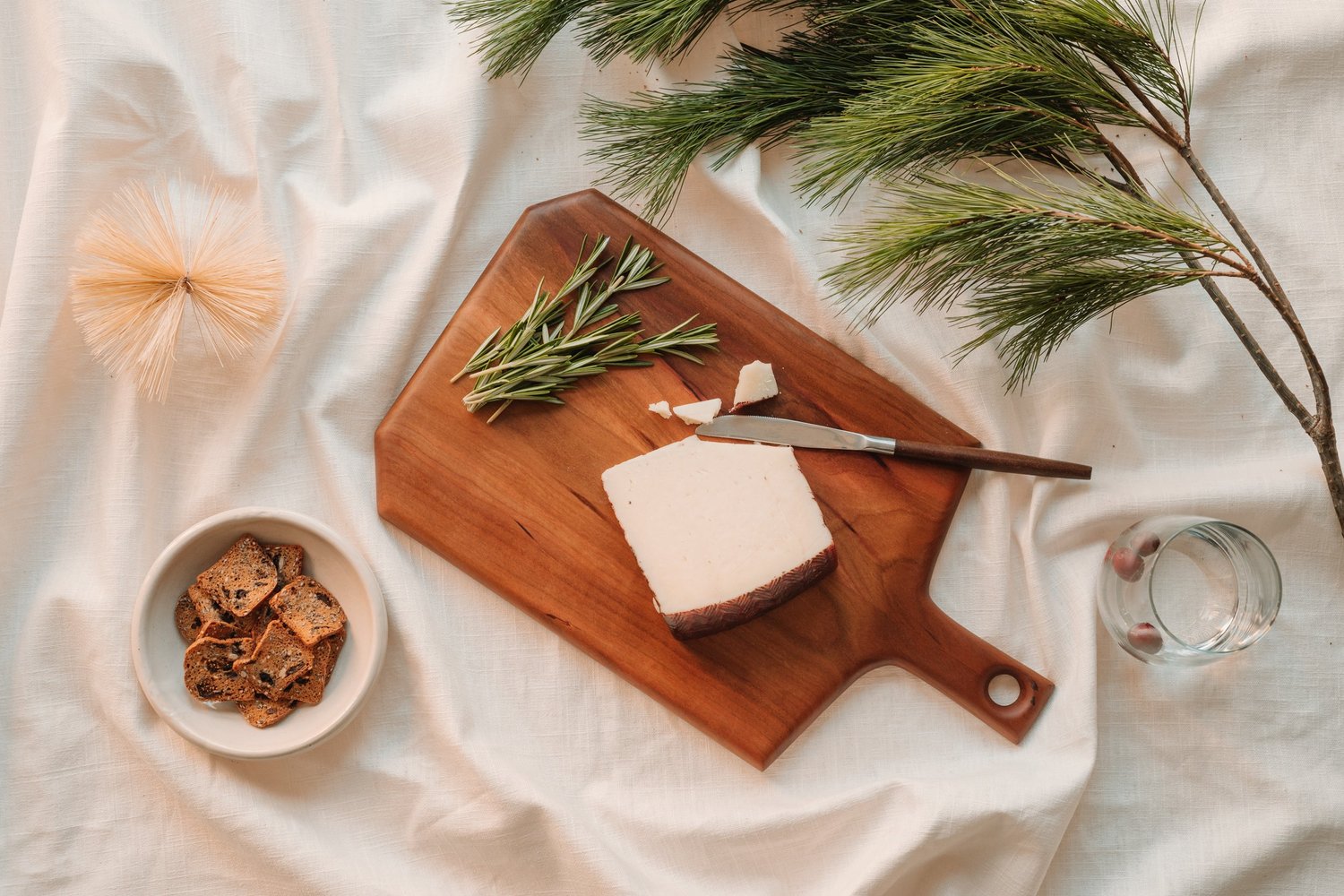 Wooden cutting board with cheese and herbs on a light fabric background