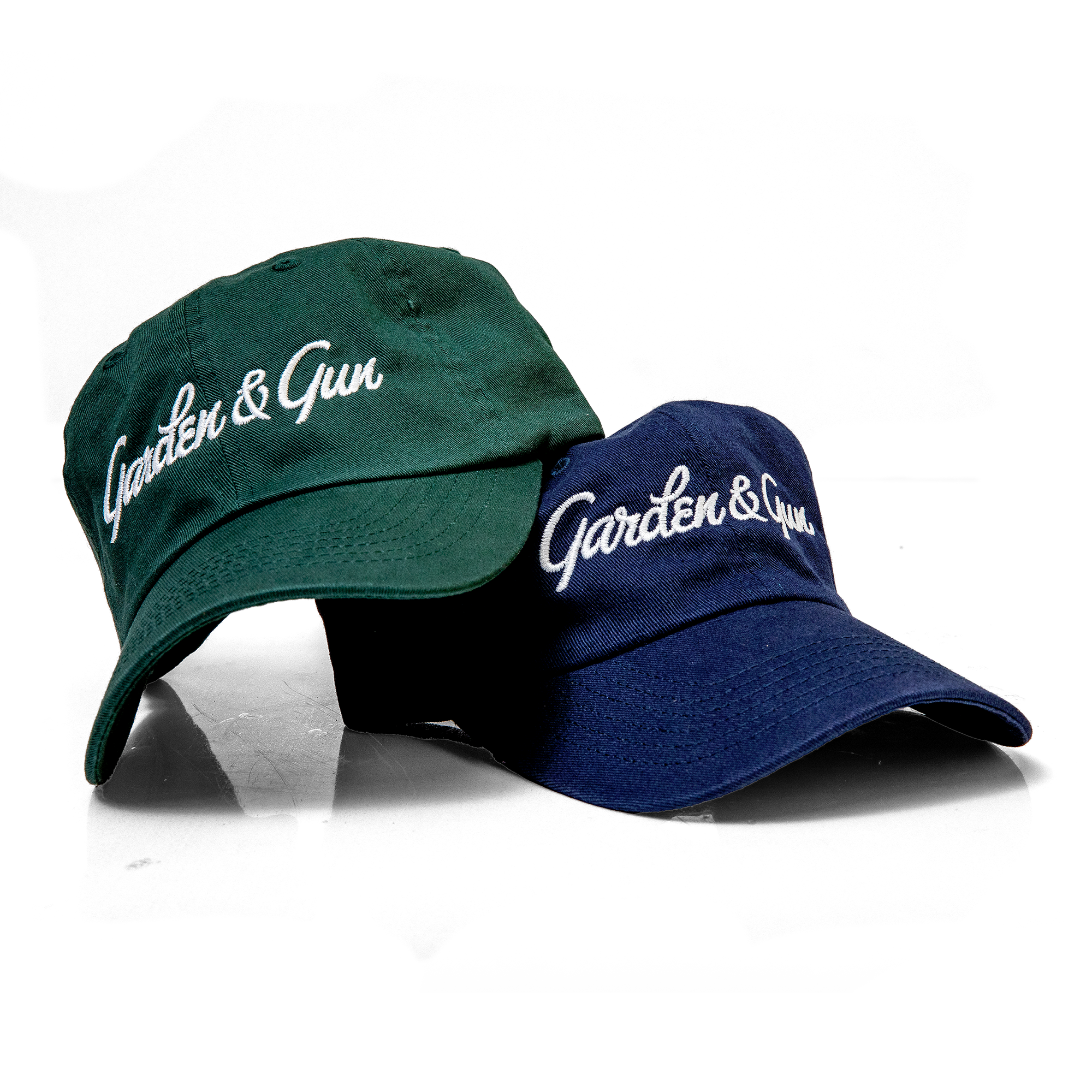 Two baseball caps, one green and one blue, with 'Garden & Gun' logo on a white background.