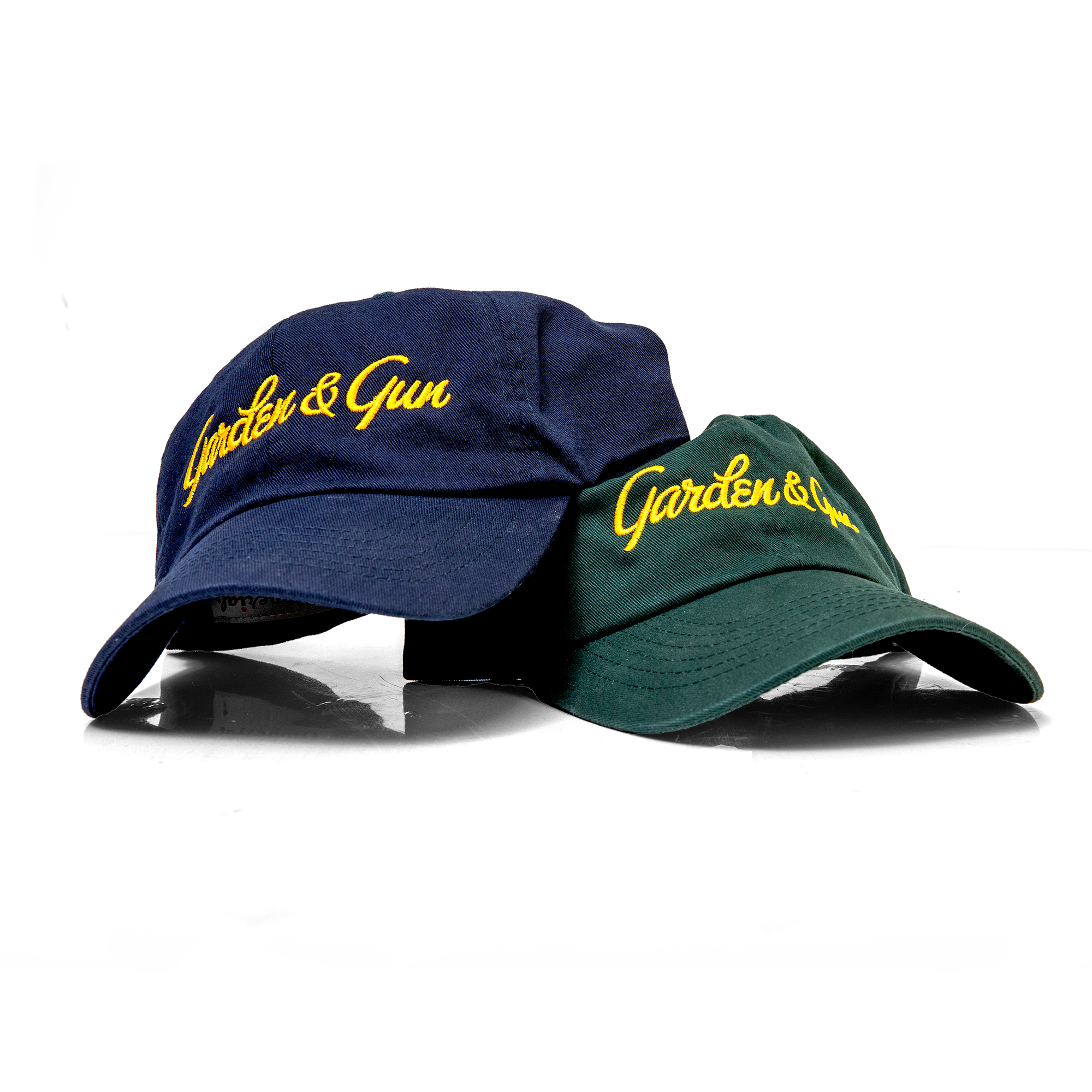 Two baseball caps, one blue and one green, with 'Garden & Gun' logo on a white background.