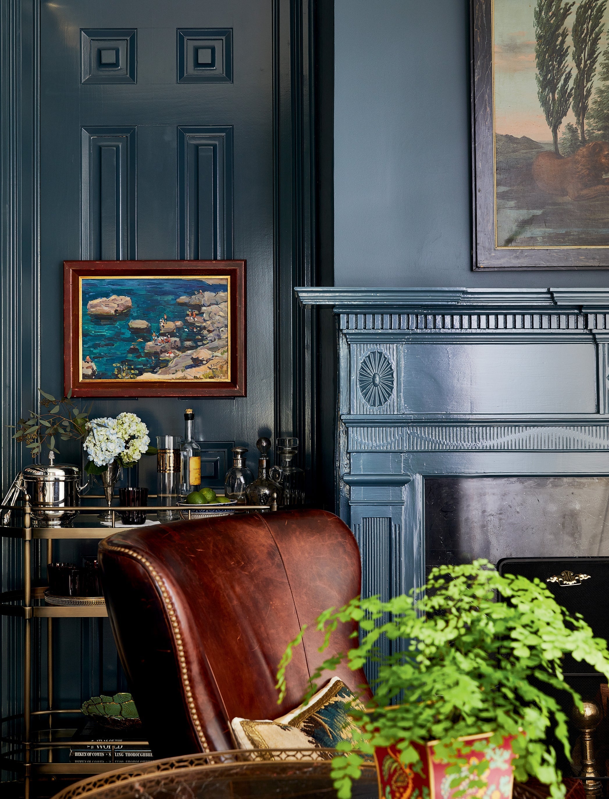 Elegant vintage-inspired home corner with a leather armchair, fireplace, and decorative touches against a blue-gray panelled wall.