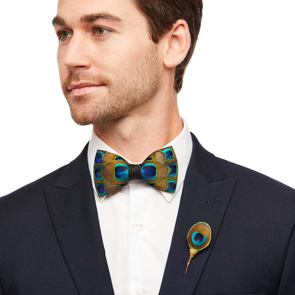 Man wearing a dark suit with a peacock feather bow tie and boutonniere on a white background