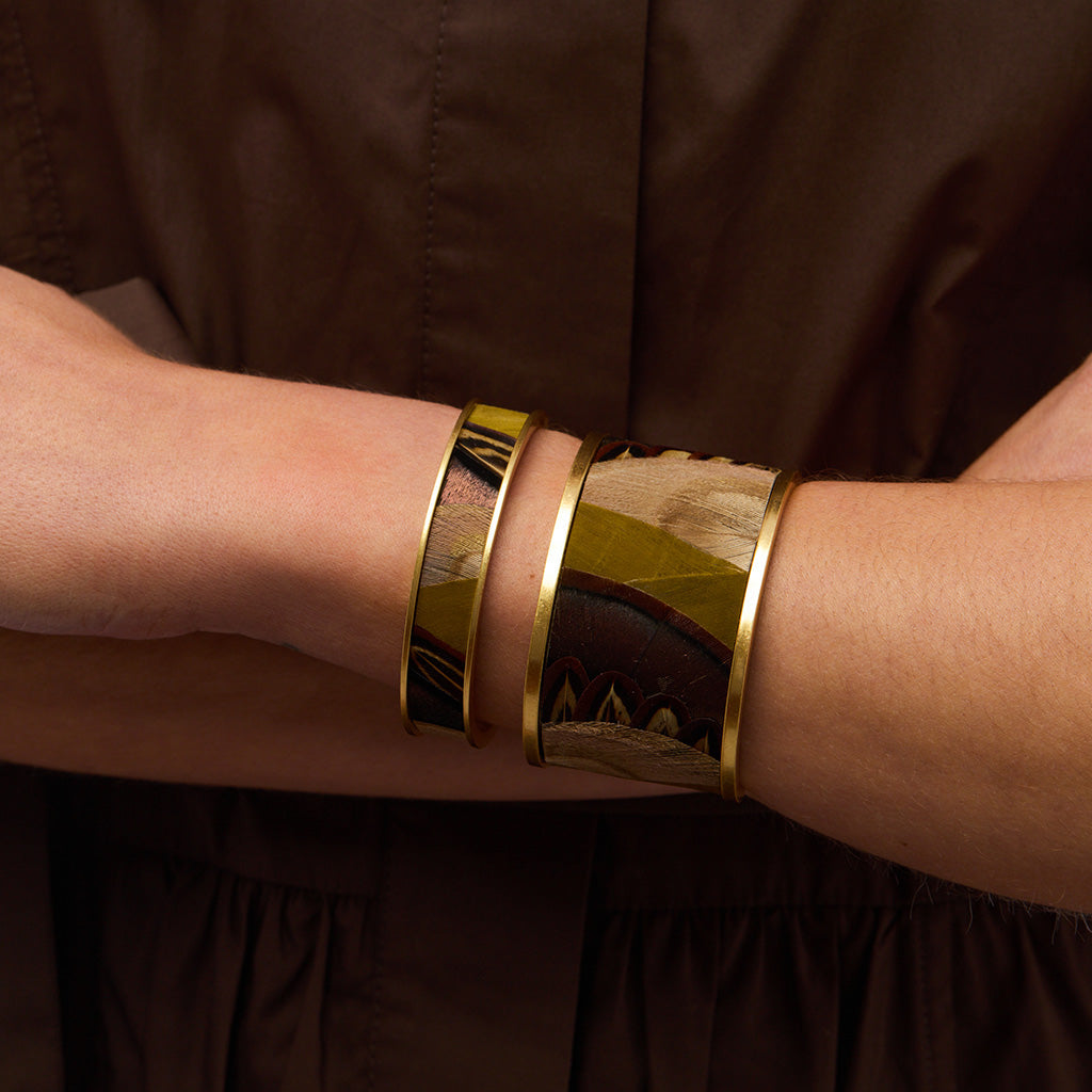 Gold bangles on a person's wrist against a brown background