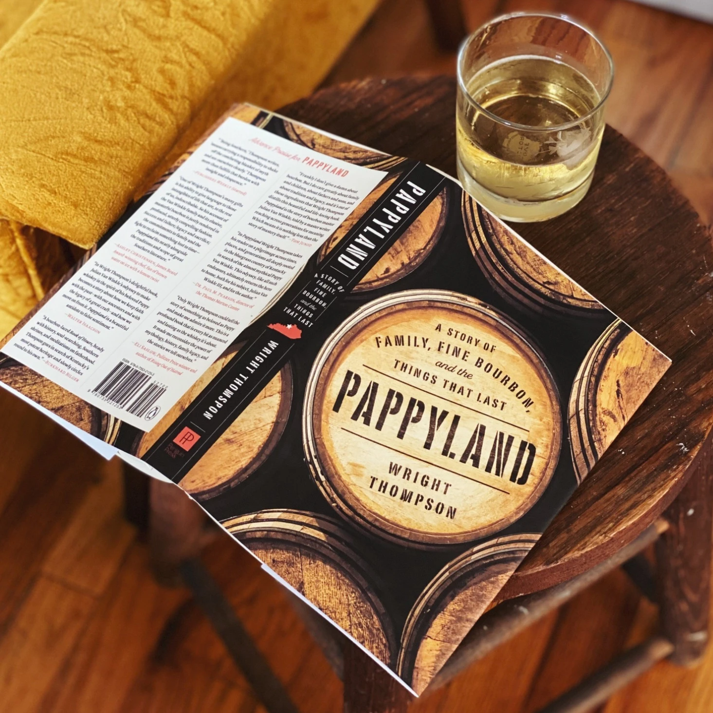 Book titled 'Pappyland' by Wright Thompson on a wooden table with a glass of liquid.