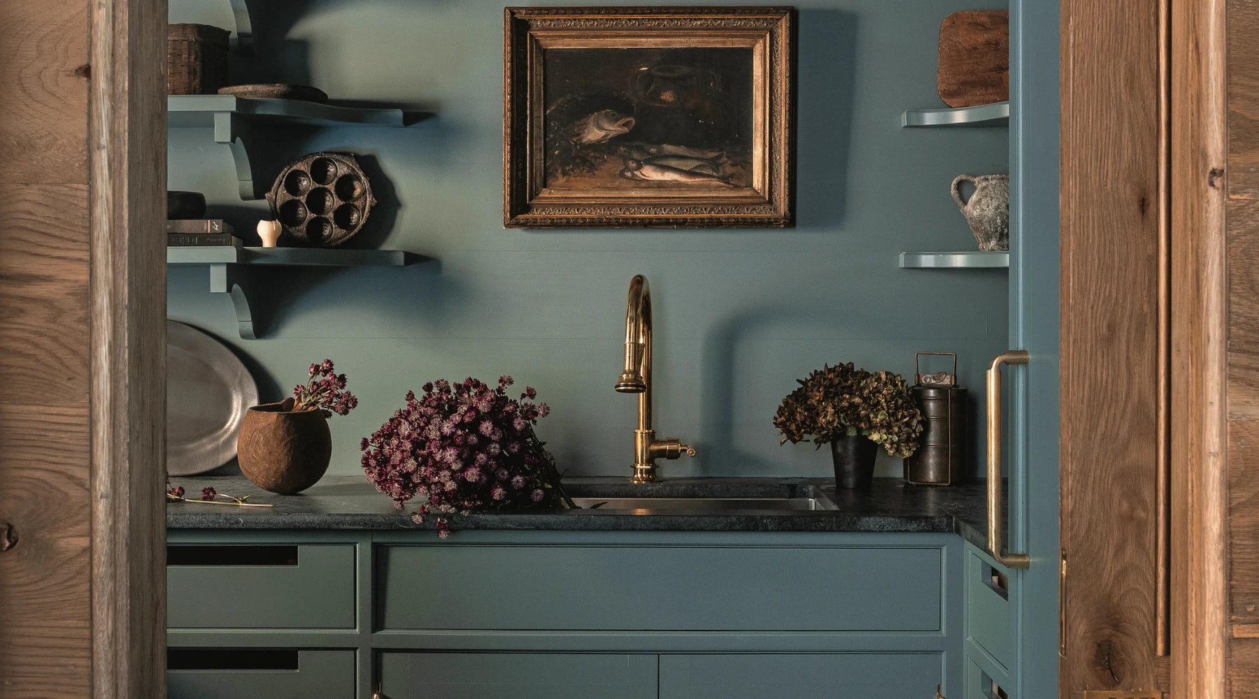 Elegant kitchen interior with teal cabinetry, brass faucet, and decorative items on open shelves inspired by Southern lifestyle.