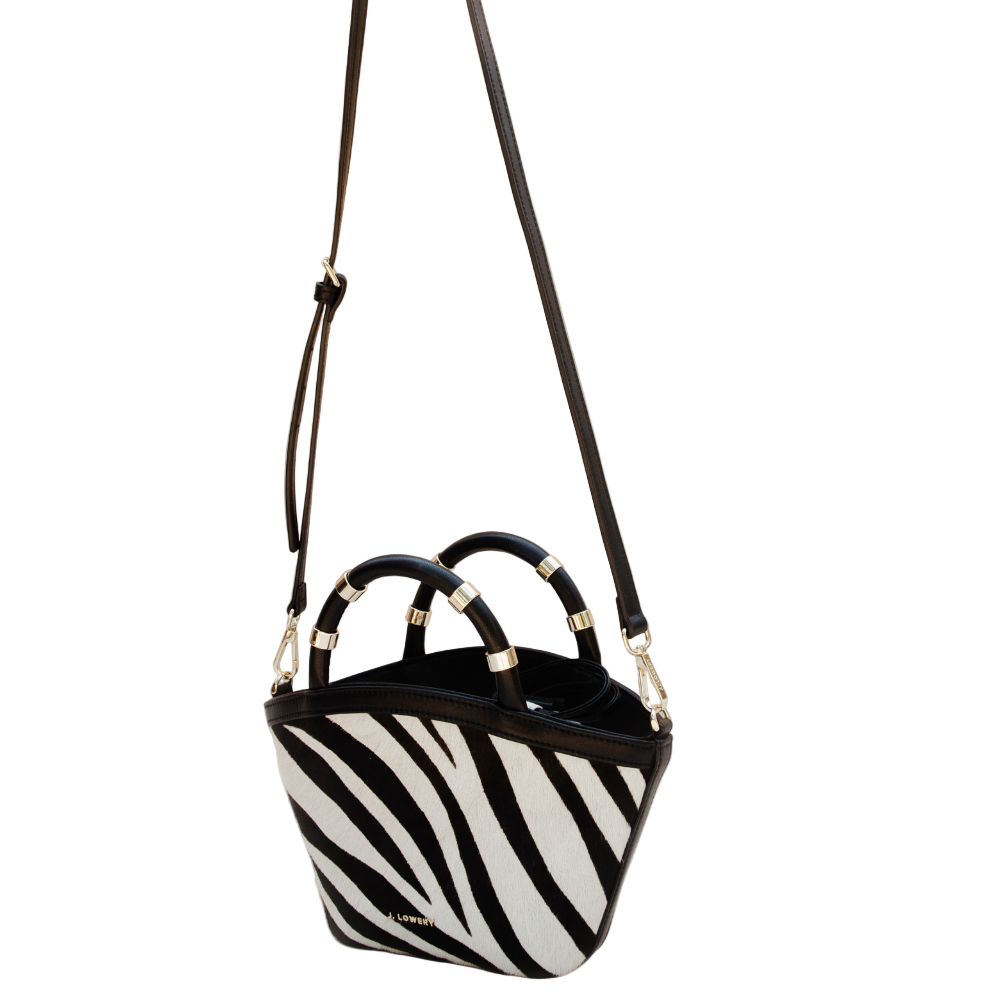 Black and white zebra-striped handbag with gold accents on a beige background
