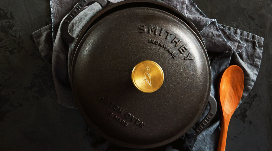 Smithey Cast Iron Dutch Oven on a dark surface on top of a dish cloth next to a wooden spoon.