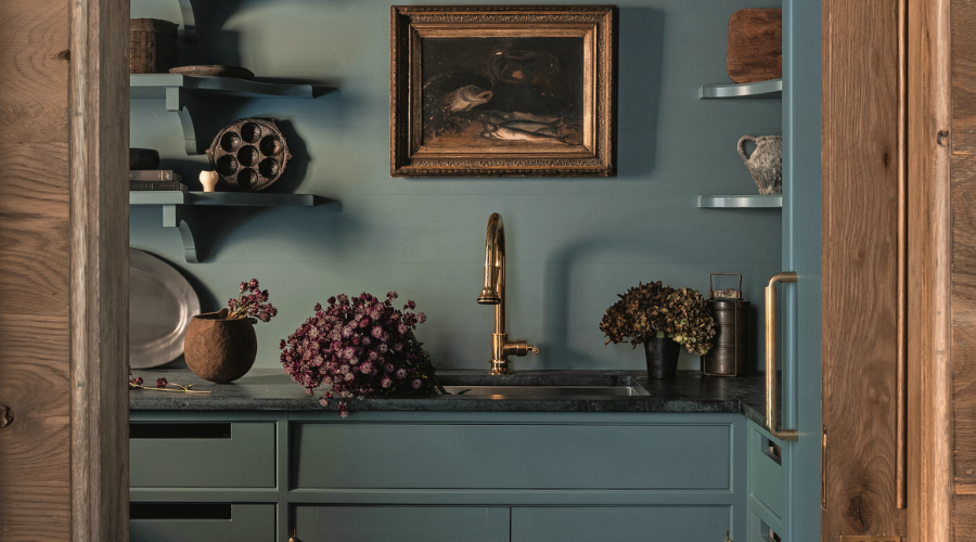 Elegant kitchen corner with dusty blue cabinets, brass fixtures, and decorative shelving.