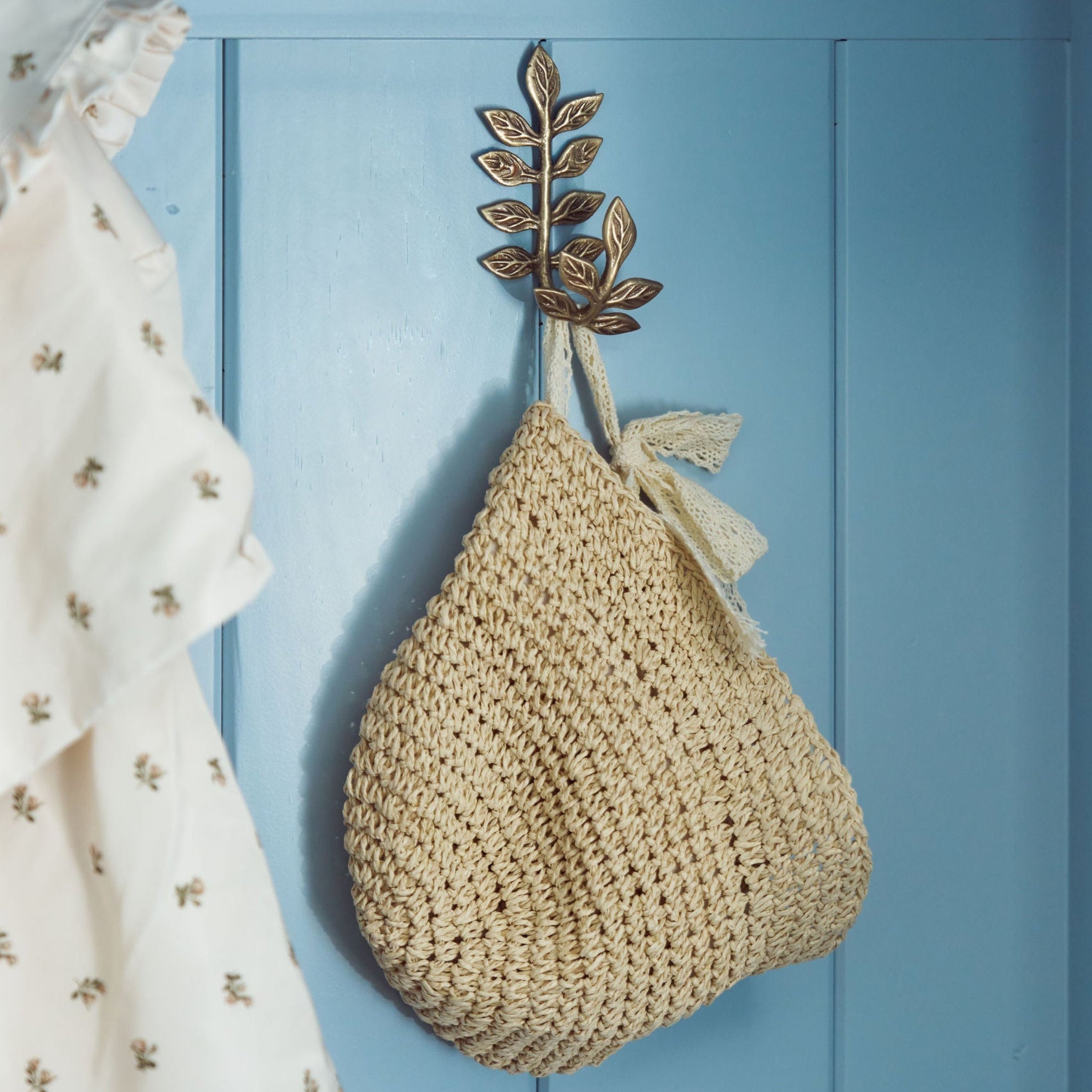 Beige woven bag hanging on a decorative hook against a light blue wall with a white dress.