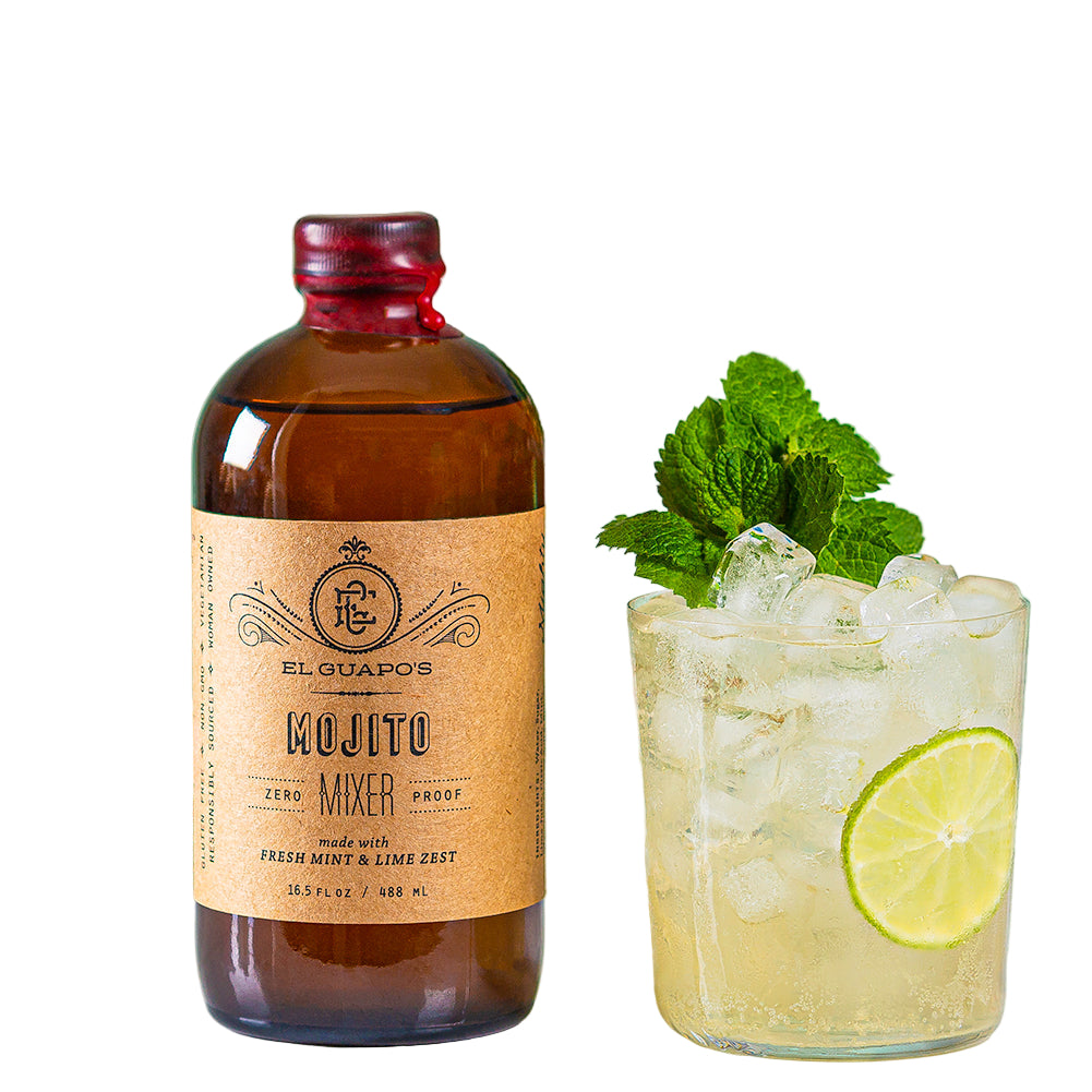 A bottle of El Guapo Mojito Mixer next to a glass filled with ice, rum, mint leaves, and a slice of lime, with a second lime beside it, all on a white surface with a green background.