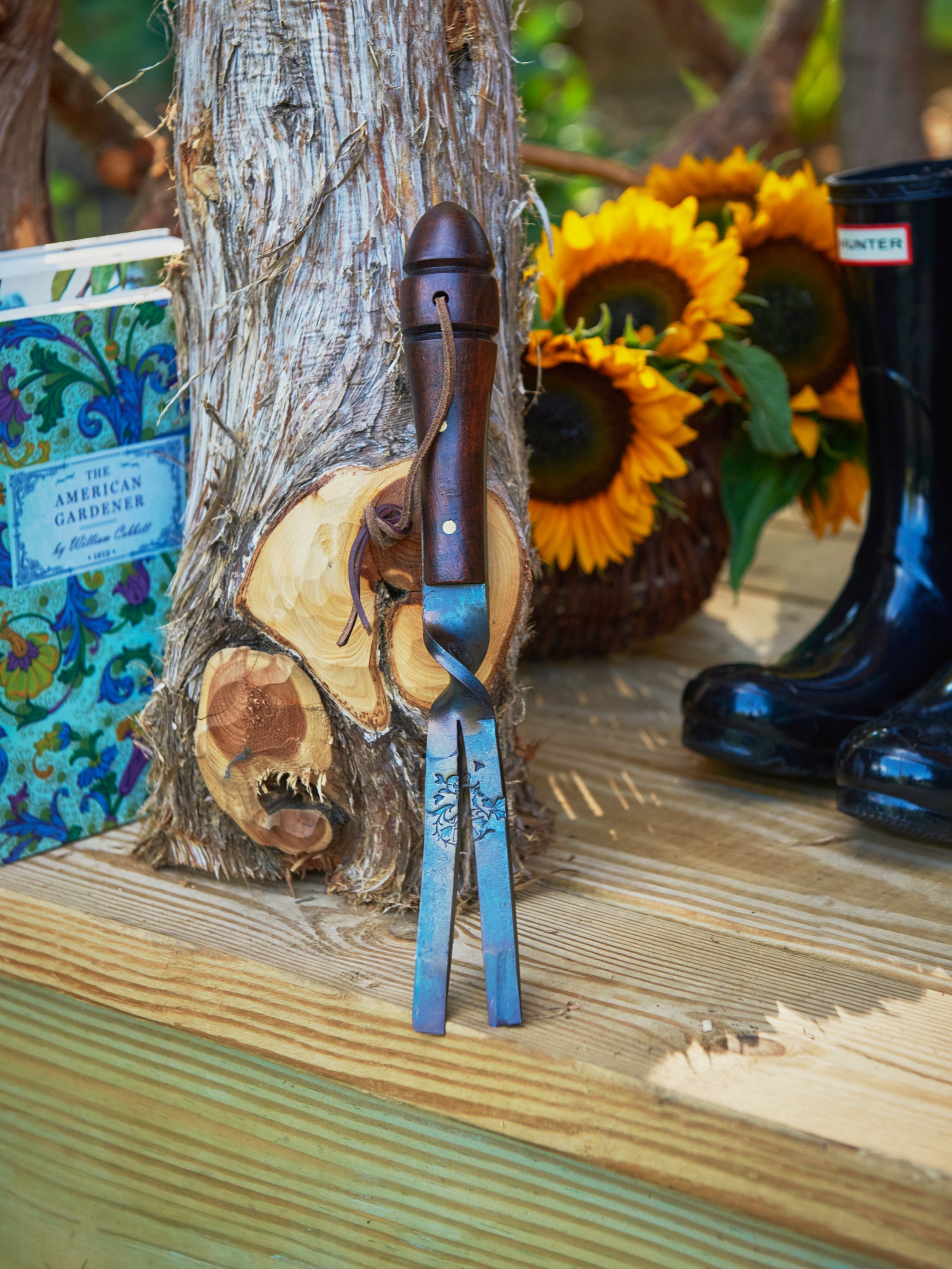 Gardening tool with wooden handle on a wooden surface next to sunflowers and boots