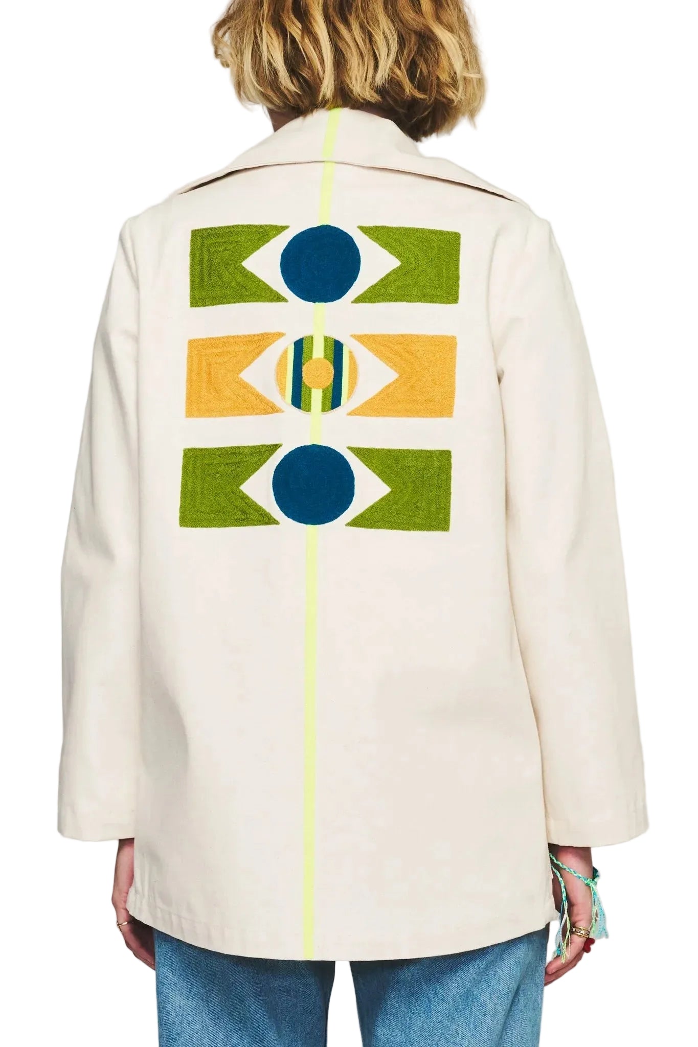 Person wearing a cream-colored coat with geometric pattern on the back, standing against a gray background.