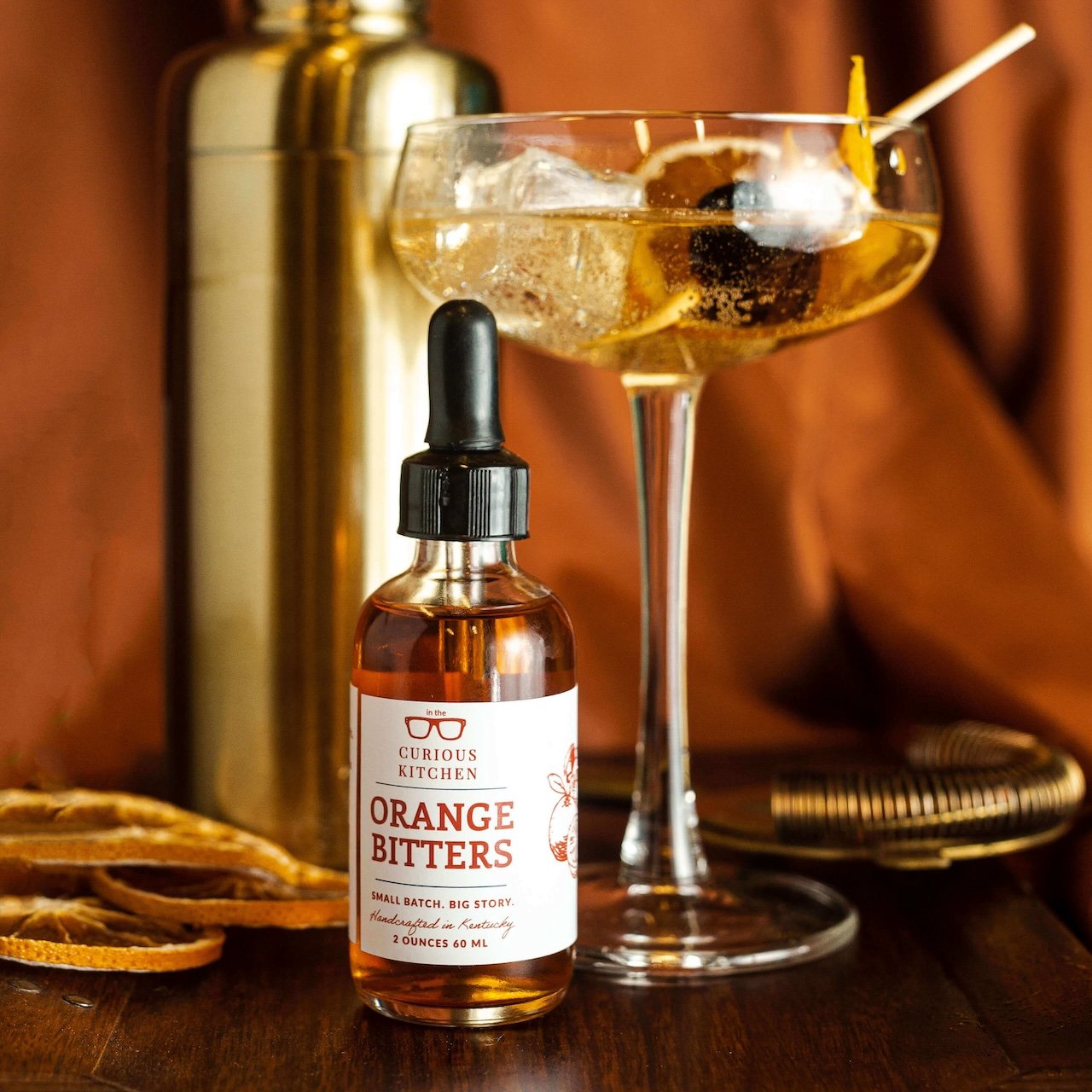 Bottle of Curious Kitchen Orange Bitters with a cocktail in the background