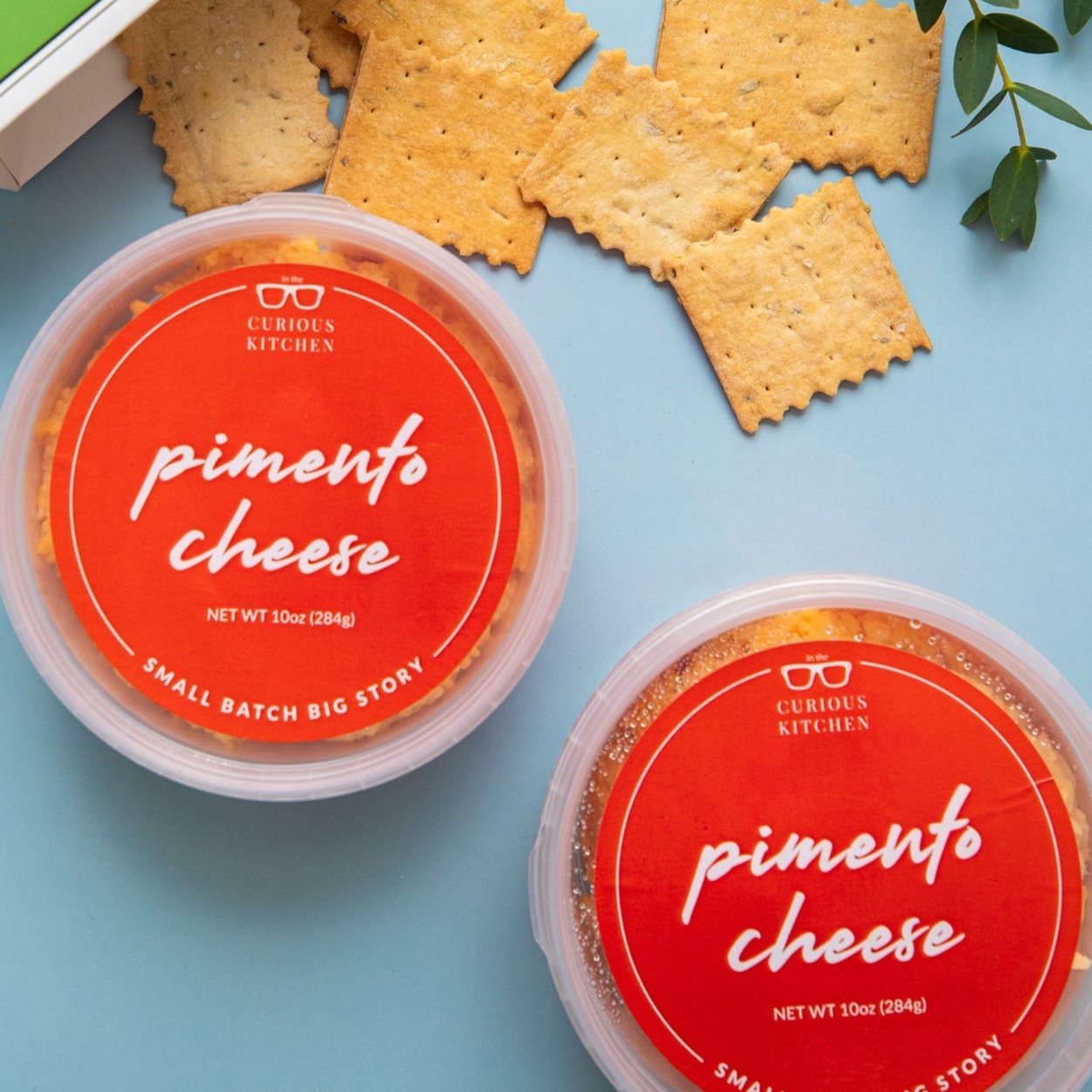 Two containers of pimento cheese with crackers on a blue background