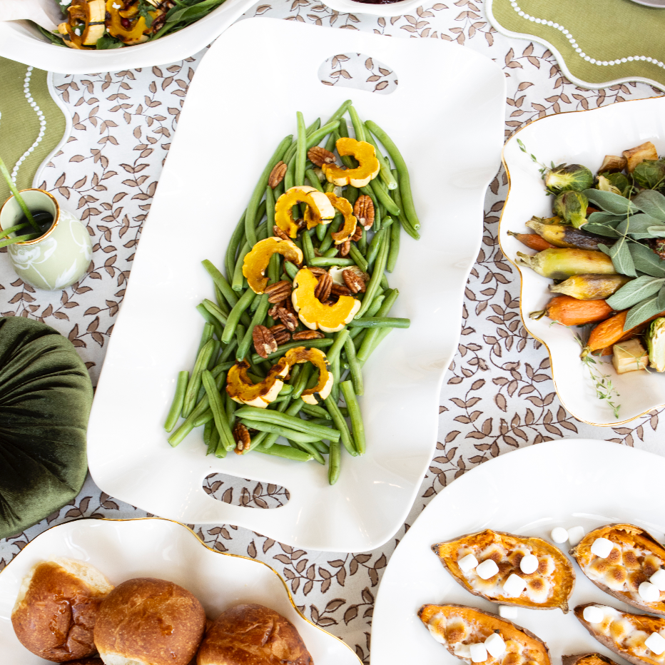 Assorted dishes including green beans with yellow squash and pecans on a patterned tablecloth.